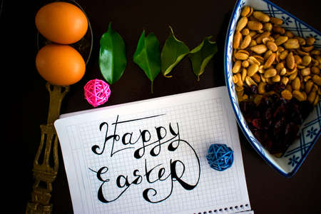 Easter flatlay on the black background with handwriting, eggs, green leaves, nuts and dry fruits, view from above.の写真素材