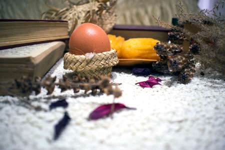 Easter composition with an egg, dry flowers and petals, wooden box and books on white backgroundの写真素材