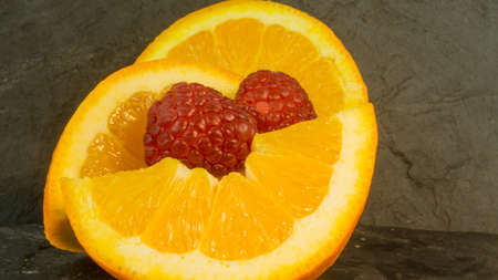 Raspberries and oranges on a background of slateの写真素材