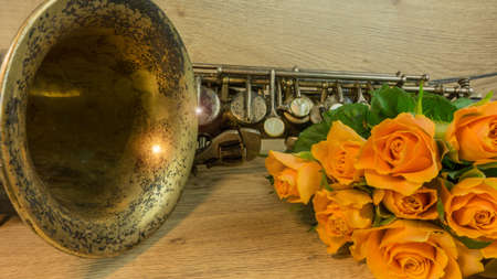 Old saxophone with roses on a wooden tableの写真素材