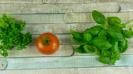 Parsley and basil with a red tomato on a wooden tableの写真素材
