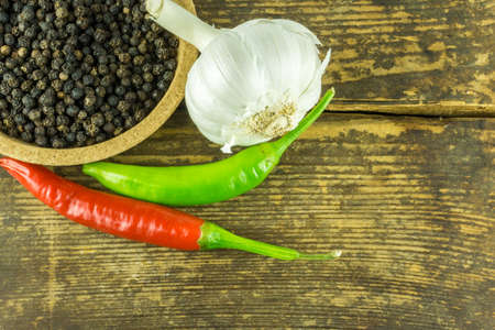 Hot peppers of different colors, black pepper and garlic on a rustic wooden backgroundの写真素材