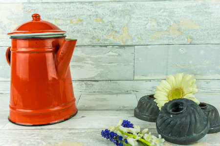 Red coffeepot with a colorful flower on a rustic white wooden backgroundの写真素材