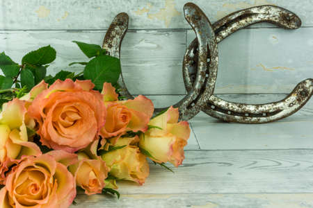 Two horseshoes with a bouquet of roses on a rustic white wooden backgroundの写真素材