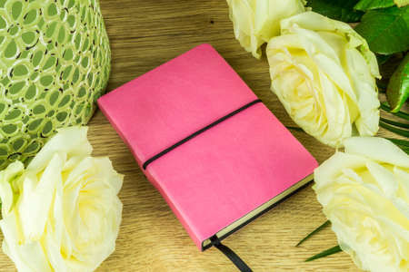White roses with a notebook on a wooden tableの写真素材