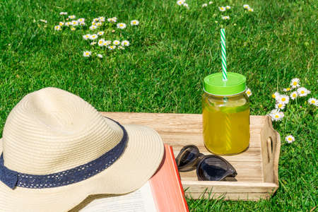 Straw hat with a book and sunglasses on a green lawnの写真素材
