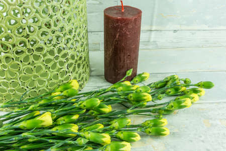 Red candle with yellow carnations on a background of woodの写真素材