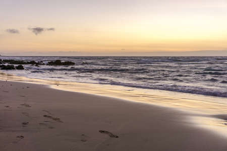 sunrise on a beach with waves and stones in the waterの写真素材