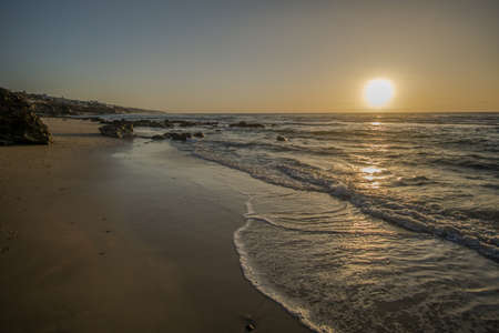 sunrise on a beach with waves and stones in the waterの写真素材