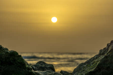 sunrise on a beach with waves and stones in the waterの写真素材
