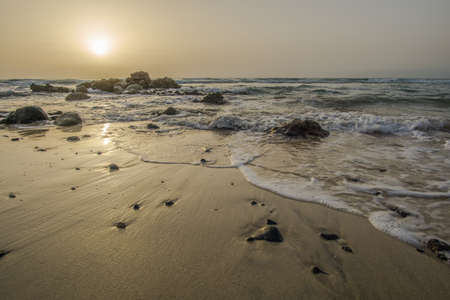 sunrise on a beach with waves and stones in the waterの写真素材