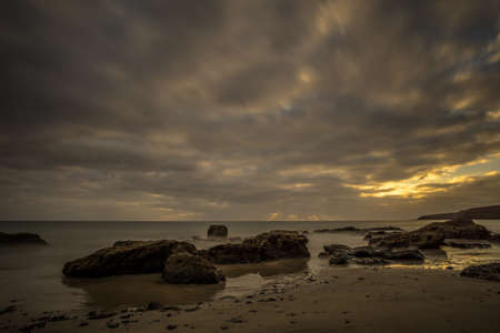 Beach on a Canarian island with dark clouds and big lava mountains at sunsetの写真素材