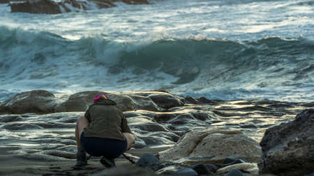 A woman with blond hair is standing on the beach and taking pictures with big wavesの写真素材