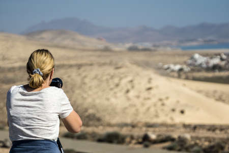 Woman with blond hair is standing on the beach and taking photosの写真素材