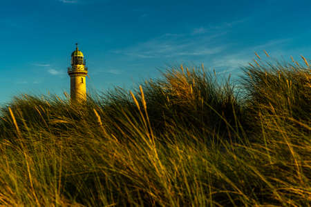 A lighthouse with dunes in the foreground at sunset and blue skyの写真素材