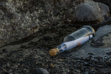 Message in a bottle on a beach with black lava rockの写真素材