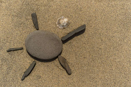 Stones in the form of a sun laid on a beach with a shell. As a backgroundの写真素材