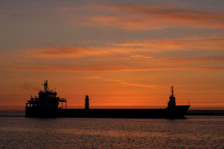 Silhouette of a big container ship at sunrise and exit from a harborの写真素材