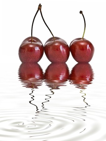 Cherries on a white background reflected on water.の写真素材
