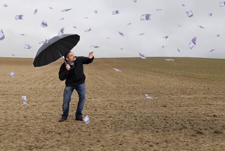 A man with an umbrella in the field amid a storm of money.