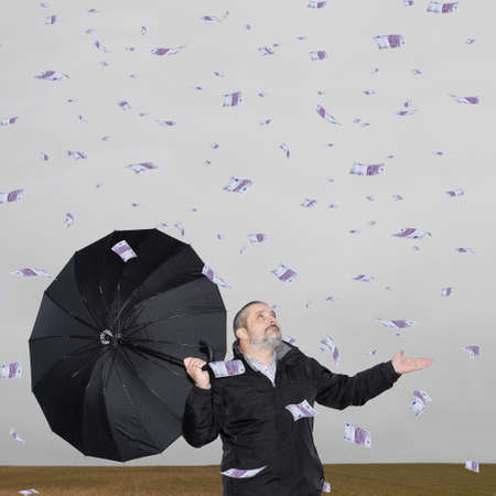 A man with an umbrella in the field amid a storm of money.