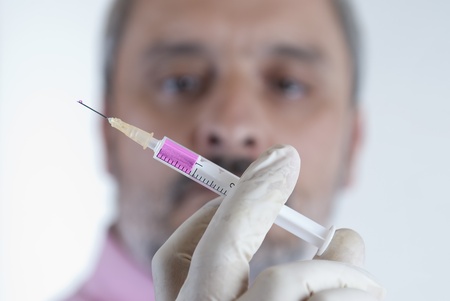 Scientific protected with mask and gloves holding a syringe filled with fluid in his laboratory.の写真素材