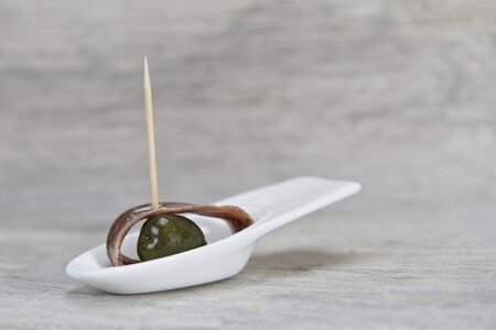 Anchovy appetizer served with green olives in a china spoon on a wooden backgroundの写真素材