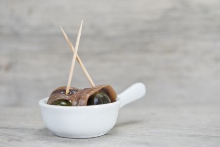 Anchovy appetizer served with green olives in a china spoon on a wooden backgroundの写真素材