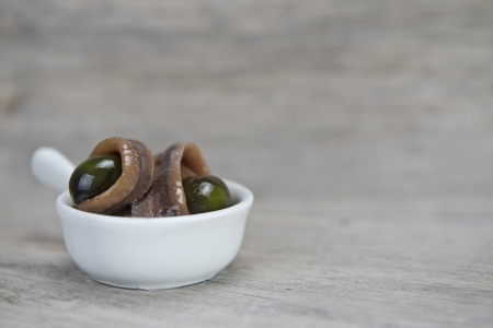 Anchovy appetizer served with green olives in a china spoon on a wooden backgroundの写真素材