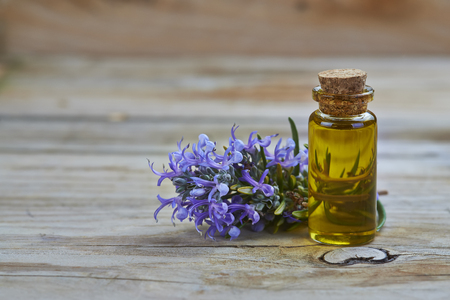 Rosemary essential oil in a small glass vial and plant with flowers on a wooden backgroundの写真素材