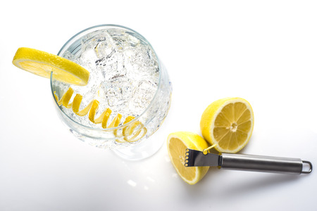 Gin and tonic in a highball cup garnished with a lemon wedge and twist