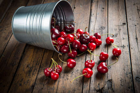 Little brass bucket of cherries on a wooden tableの写真素材
