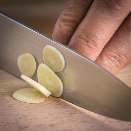 Chef slicing garlic cloves on the cutting board with a knife