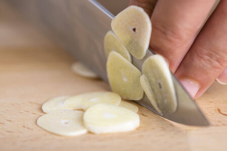 Chef slicing garlic cloves on the cutting board with a knifeの写真素材