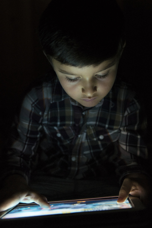 Child playing with a tablet pc and illuminated by its screenの写真素材