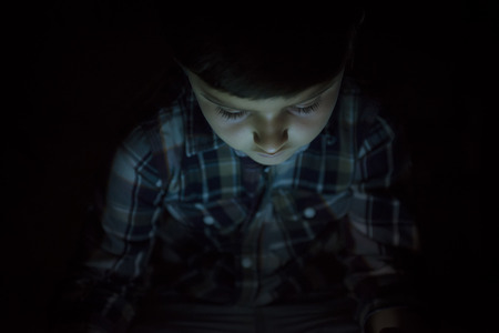 Child playing with a tablet pc and illuminated by its screenの写真素材