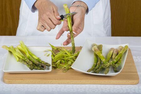 Trim and peel asparagus in the kitchen by a chef doing it with her hands and a manual peelerの写真素材