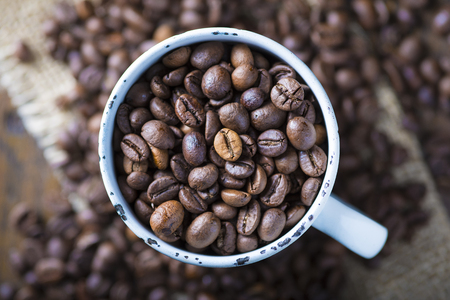 Roasted coffee beans in a porcelain cup on a burlapの写真素材