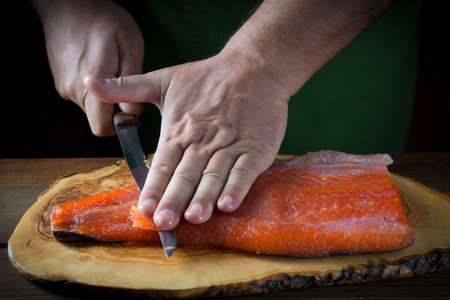 Slicing gravlax salmon with a knife on a cutting boardの写真素材