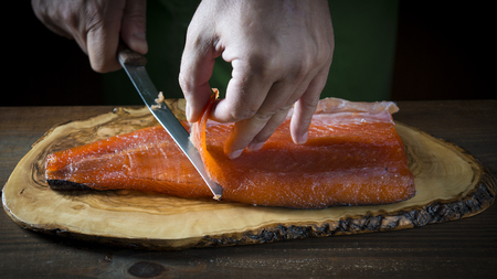 Slicing gravlax salmon with a knife on a cutting boardの写真素材
