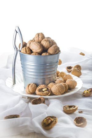 Bucket full of walnuts with a nutcracker on a wooden white backgroundの写真素材
