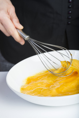Chef beating chicken eggs in a bowl witha a manual mixerの写真素材