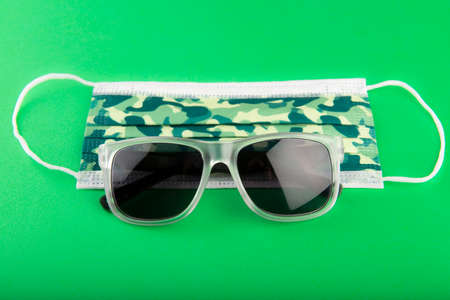 Surgical camo facemask and sunglasses on a green backgroundの写真素材