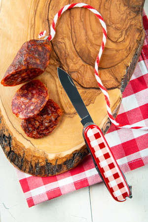 Cutting chorizo with a swiss army knife on a wooden board and vichy clotheの写真素材