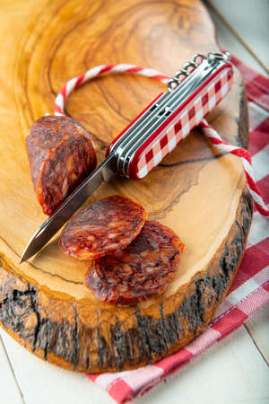 Cutting chorizo with a swiss army knife on a wooden board and vichy clotheの写真素材