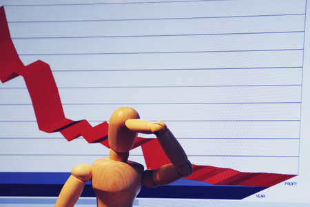 Wooden human mannequin putting his hand on his head with a graph of economic losses.