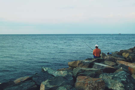 Fisherman at sunset on a breakwater in Constanta, Romania. Fisherman relaxing practicing sport...