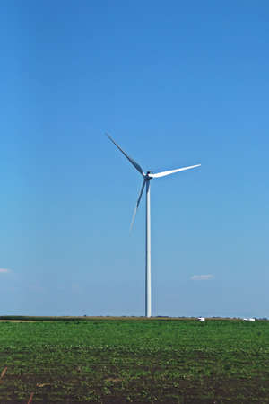 Electric wind turbine between farm fields in Romania. Wind turbine with a blue sky in the...