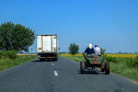 Ion Corvin / Romania; 06/07/2018. Rural road next to farm fields. Truck overtaking an old horse carriage that is driving along the side of the road.のeditorial素材