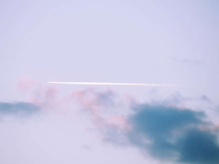 The wake of an airplane at sunset. Airplane flying in the sky barely visible in the distance but...